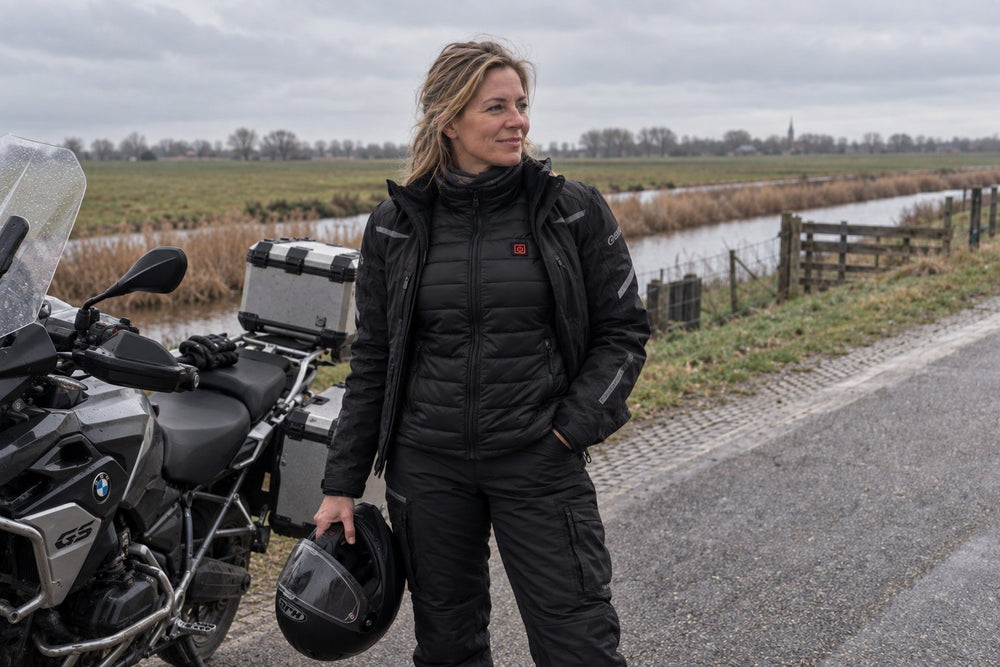 Motorrijder in verwarmde kleding naast haar motor op de dijk